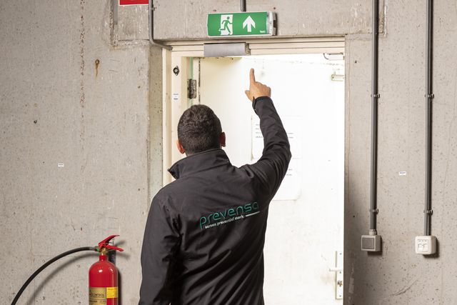 Adviseur van Prevensa wijst op de vluchtrouteaanduiding boven een nooduitgang