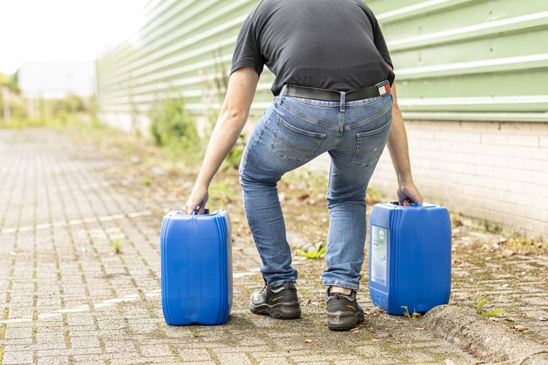 Medewerker tilt twee jerrycans, een voorbeeld van fysieke belasting